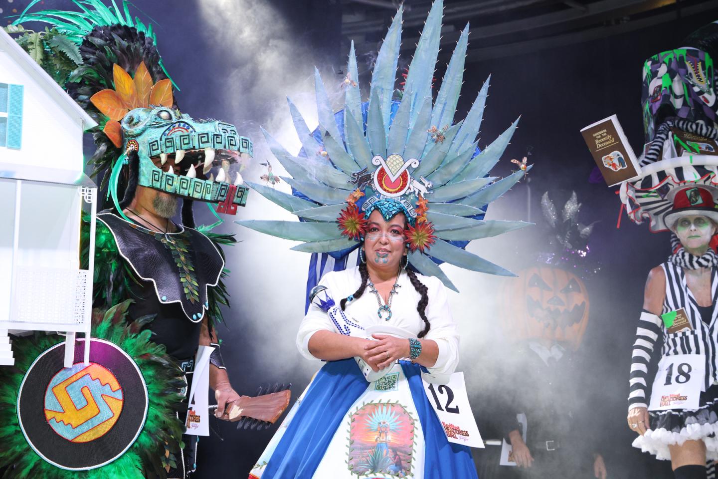 Three performers in elaborate Aztec-inspired feathered headdresses and costumes.