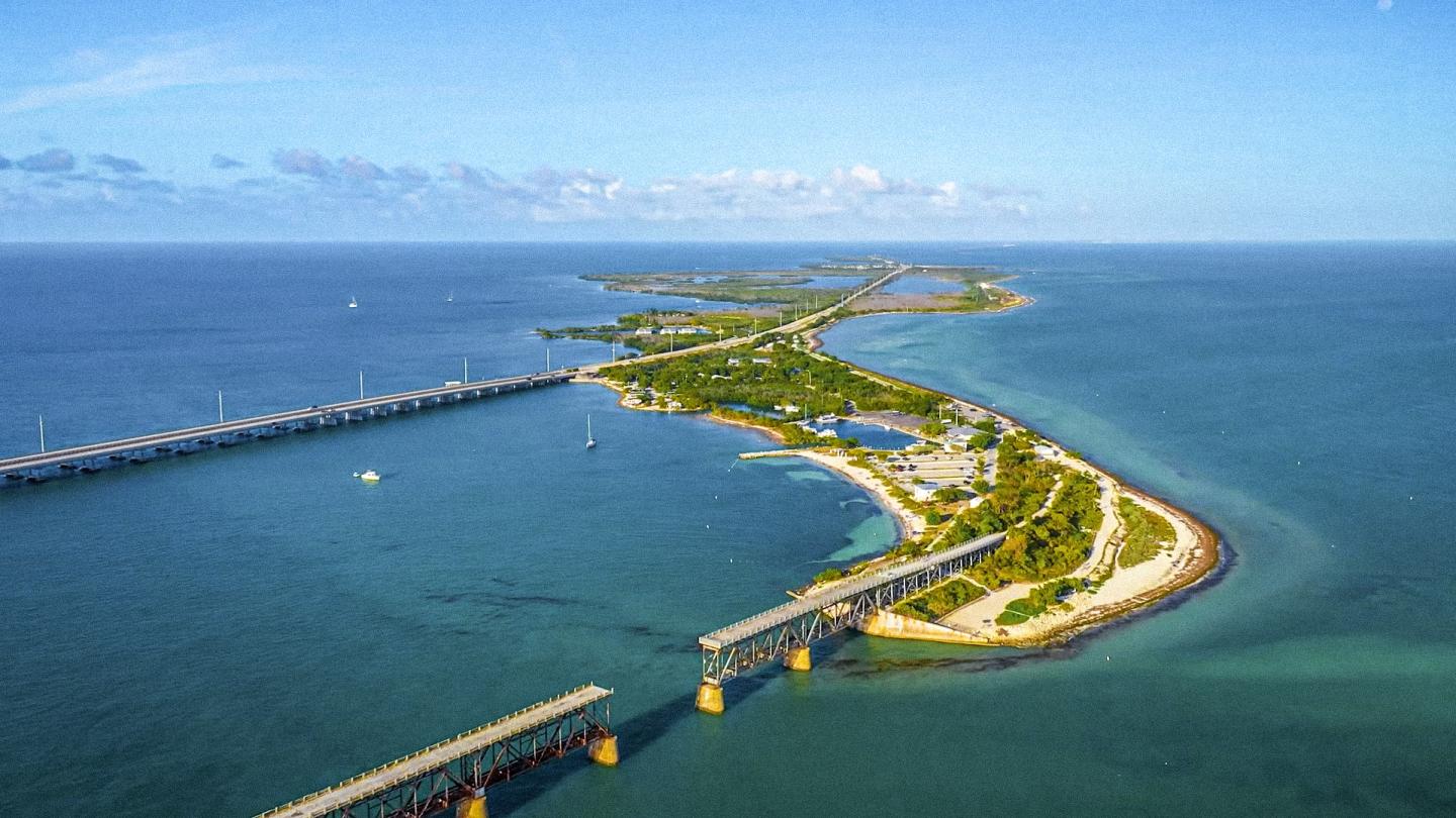 Aerial view of a winding coastal bridge and green island chain over blue water.