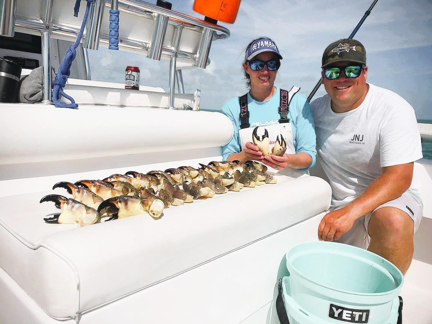 Two men on a boat display a row of freshly caught crab legs.