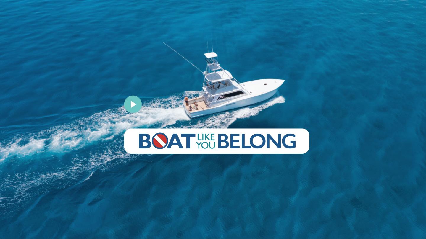 White boat cruising on blue water, towing a “Boats Belong” banner.