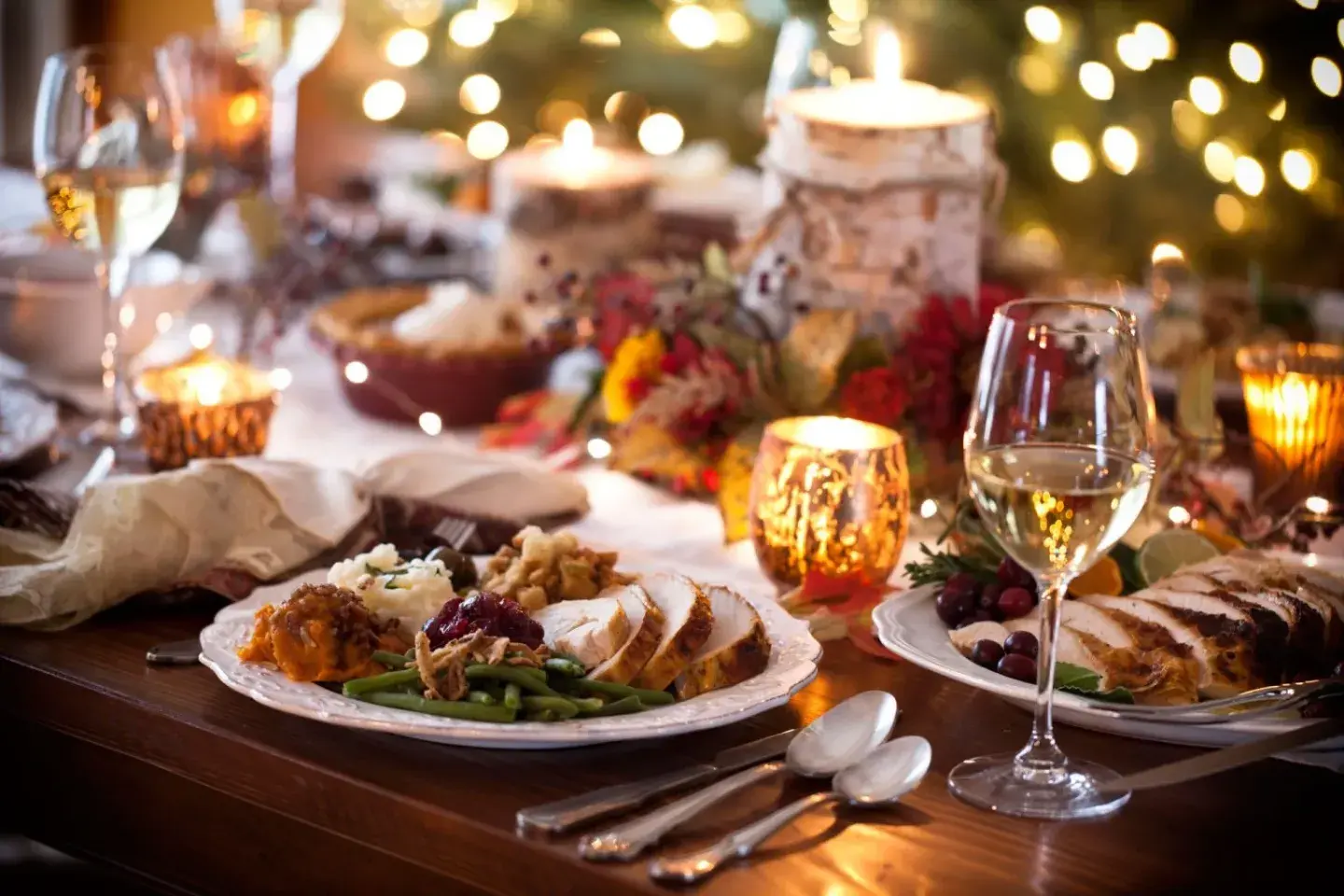 Festive candlelit dinner table with roast turkey, wine glasses, and holiday lights.