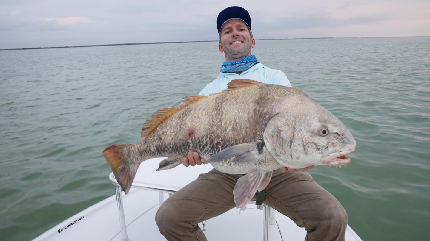 Man holding a large fish on a boat at sea.