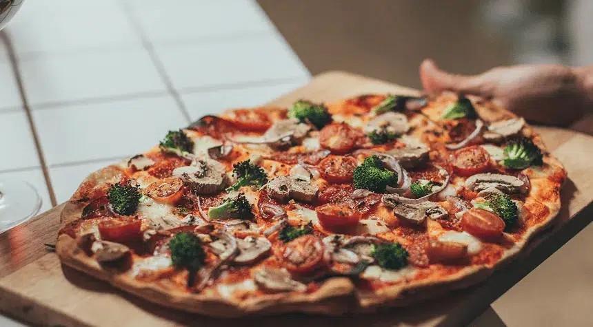 Freshly baked vegetable pizza on a wooden board, held by hands.
