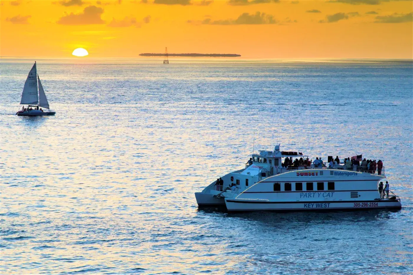 Passenger ferry and sailboat on a sunlit sea at sunset.