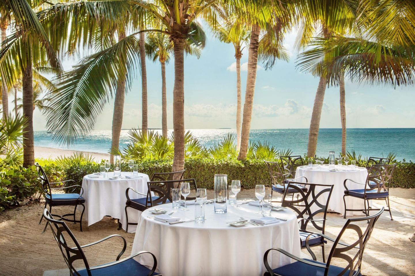Beachside restaurant tables beneath palm trees overlooking the ocean