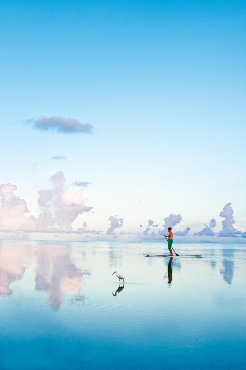 Person paddleboarding on a calm blue lake beneath soft clouds