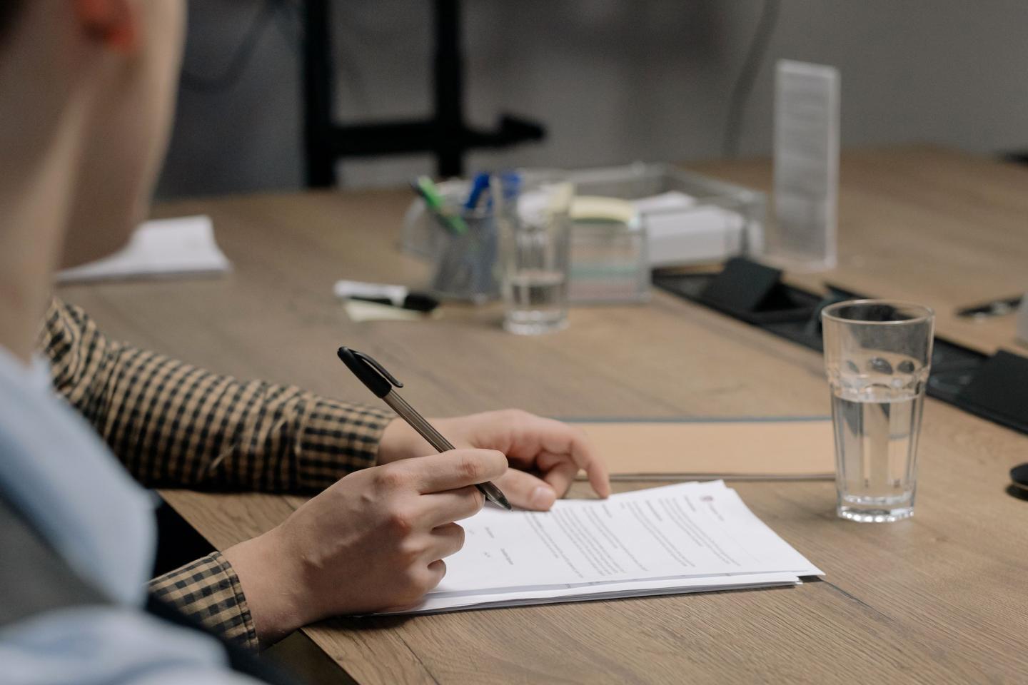 Two people reviewing and signing documents at a desk with a glass of water.