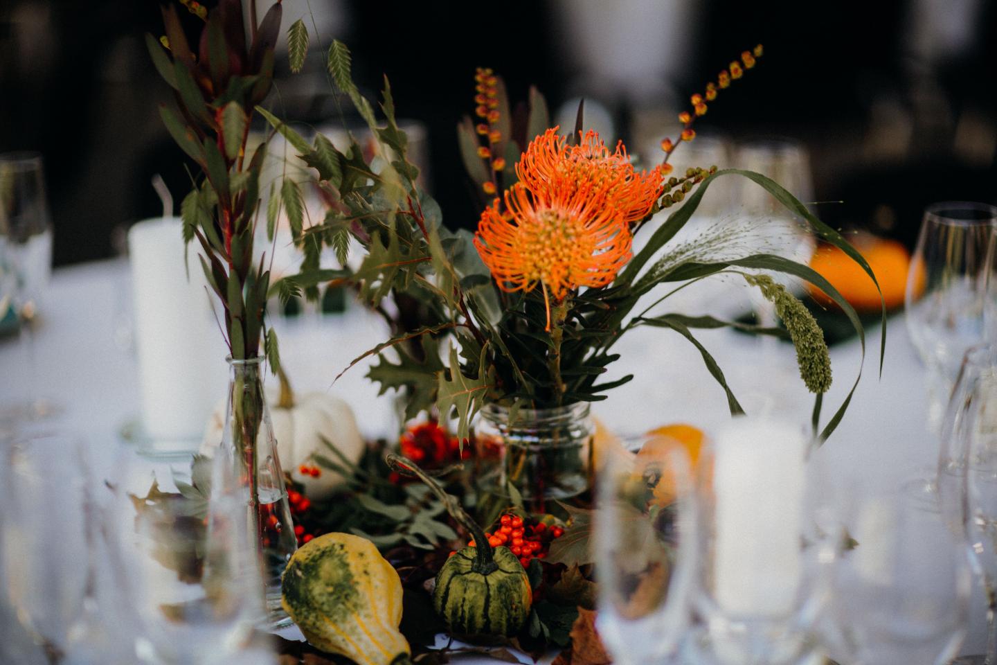 Floral centerpiece with orange pincushion protea on a white-clothed table.