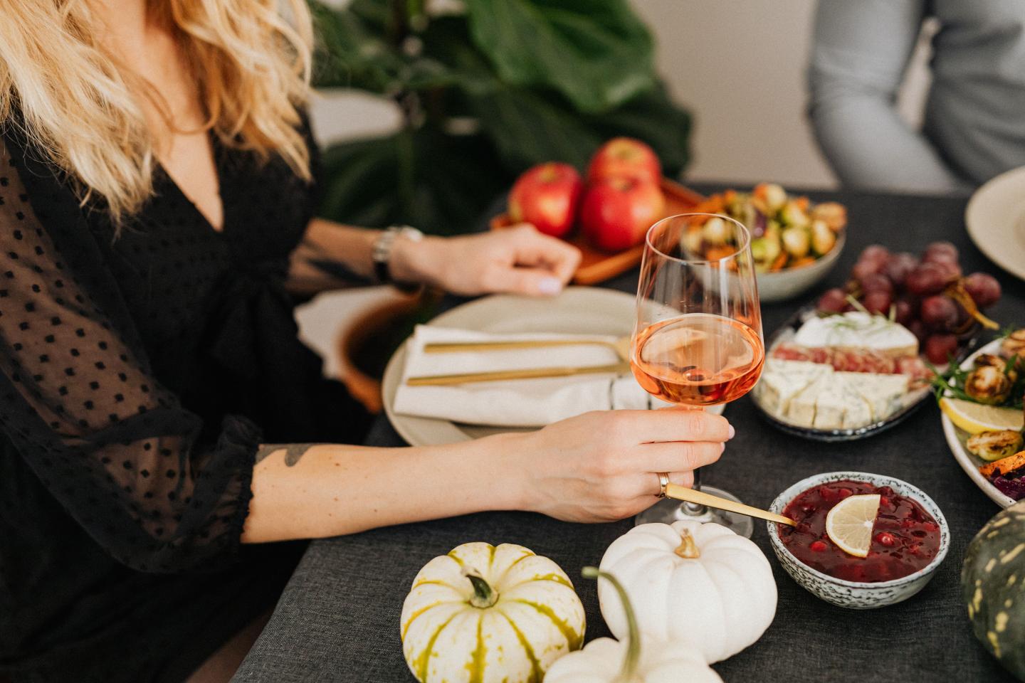 Woman setting a festive autumn dinner table with pumpkins, wine, and dishes