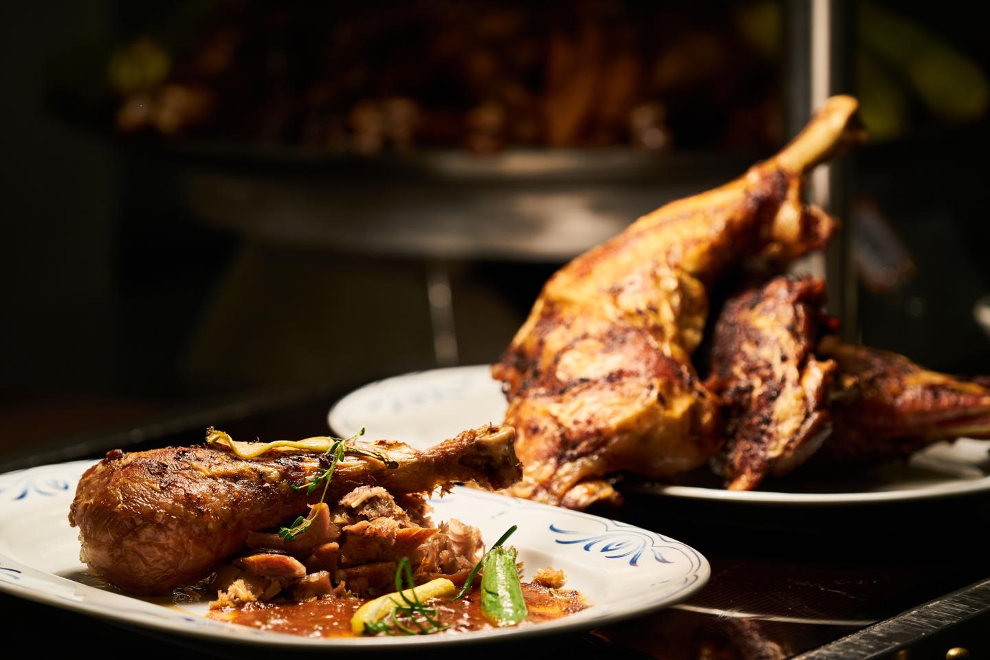 Roasted bird on a platter beside a plate of meat and vegetables.
