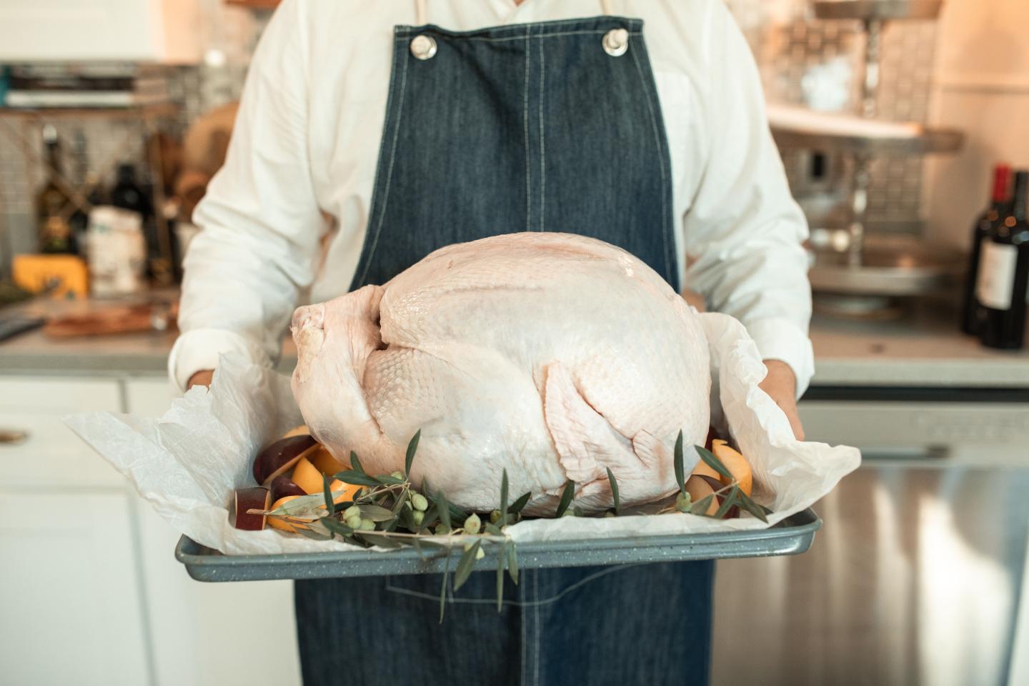 Chef holding a raw turkey on a tray in a kitchen.