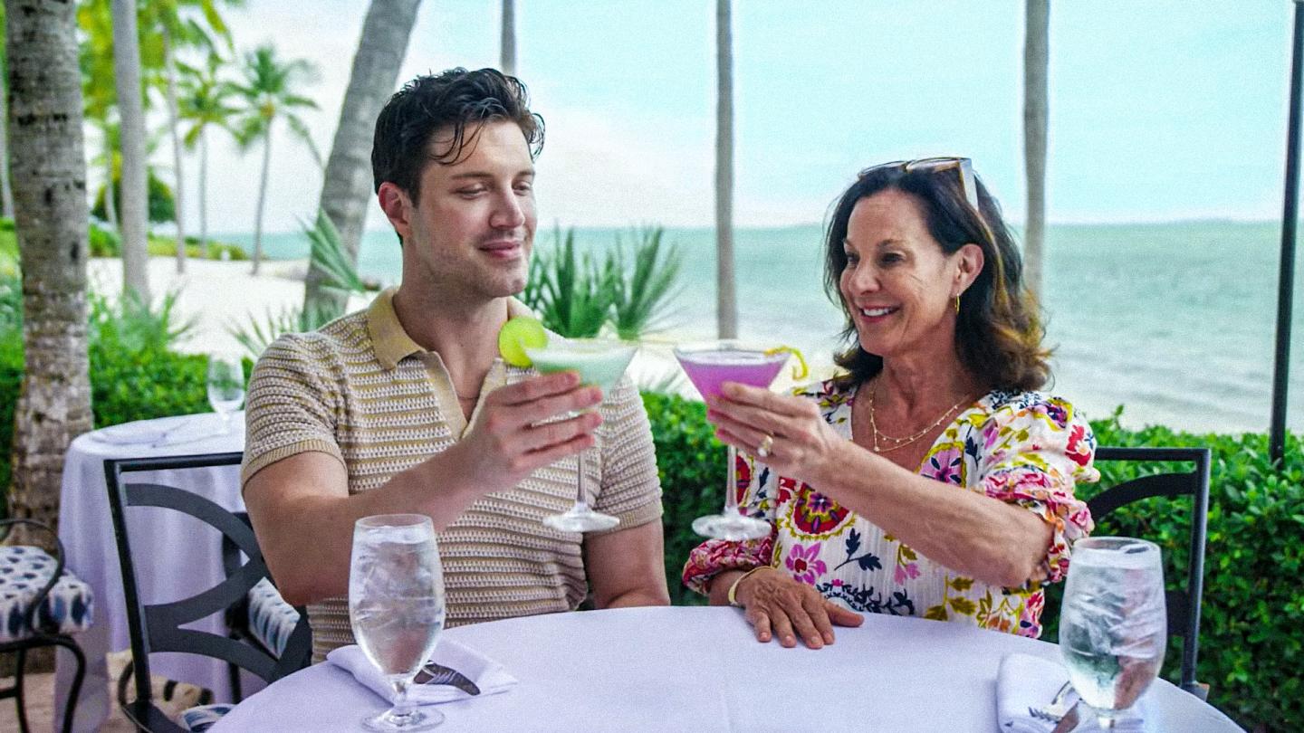 Couple toasting with tropical drinks at an oceanfront restaurant.
