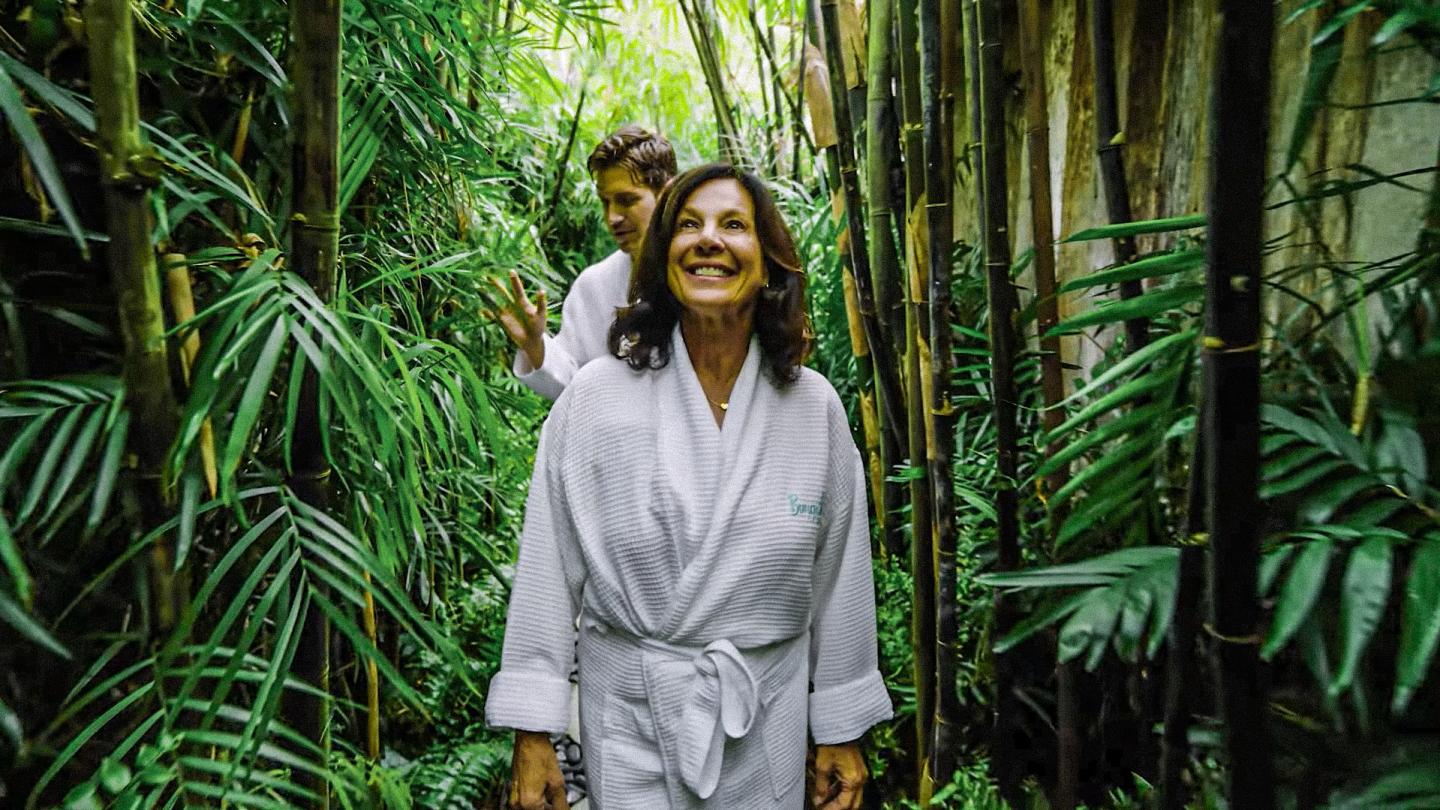 Smiling woman in white walking through a lush bamboo forest