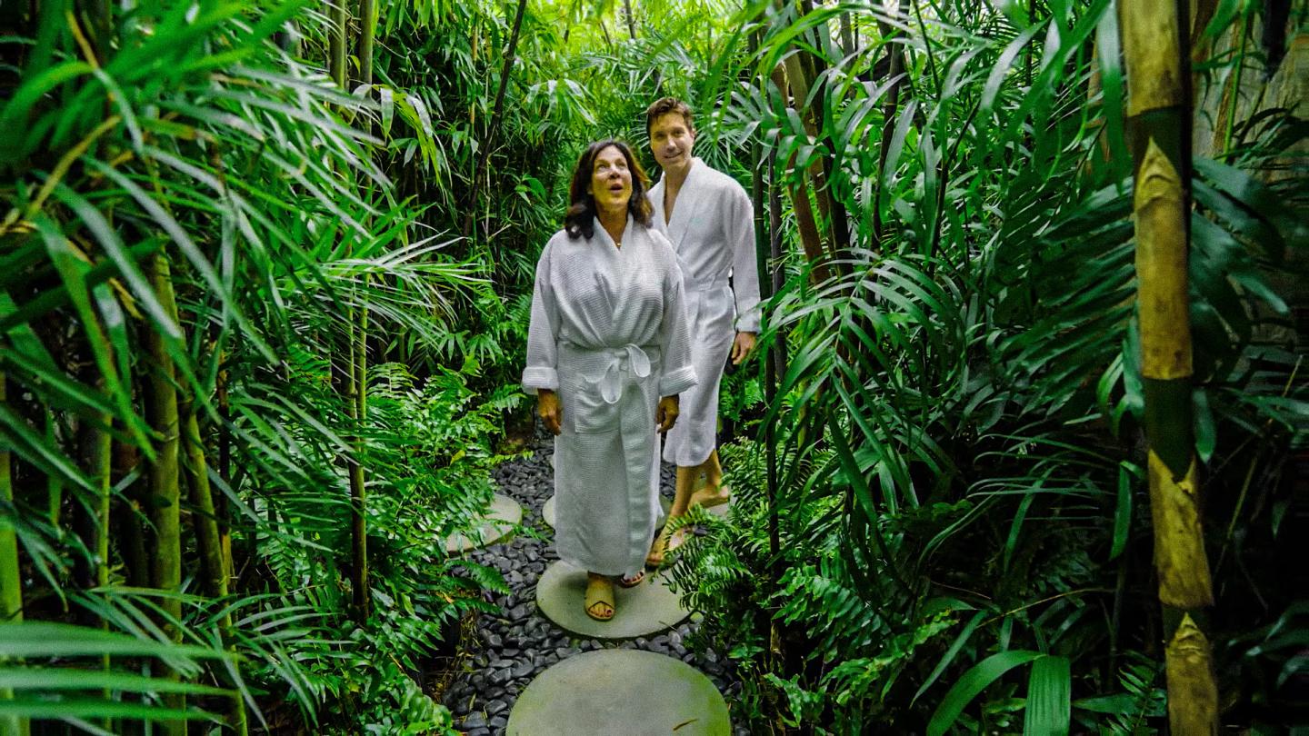 Couple in white robes walking a stone path through lush tropical jungle