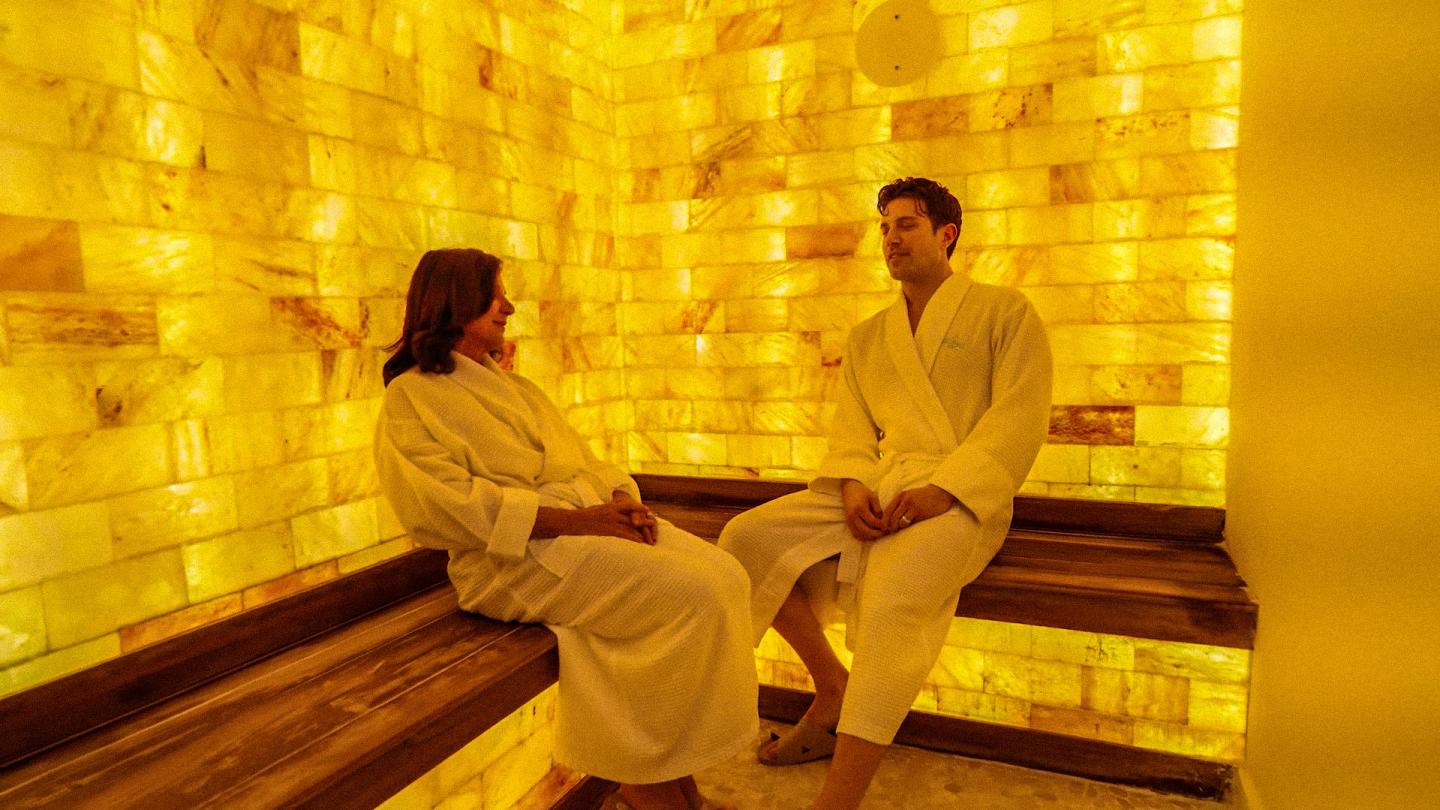 Two people seated in a glowing yellow glass-brick room.