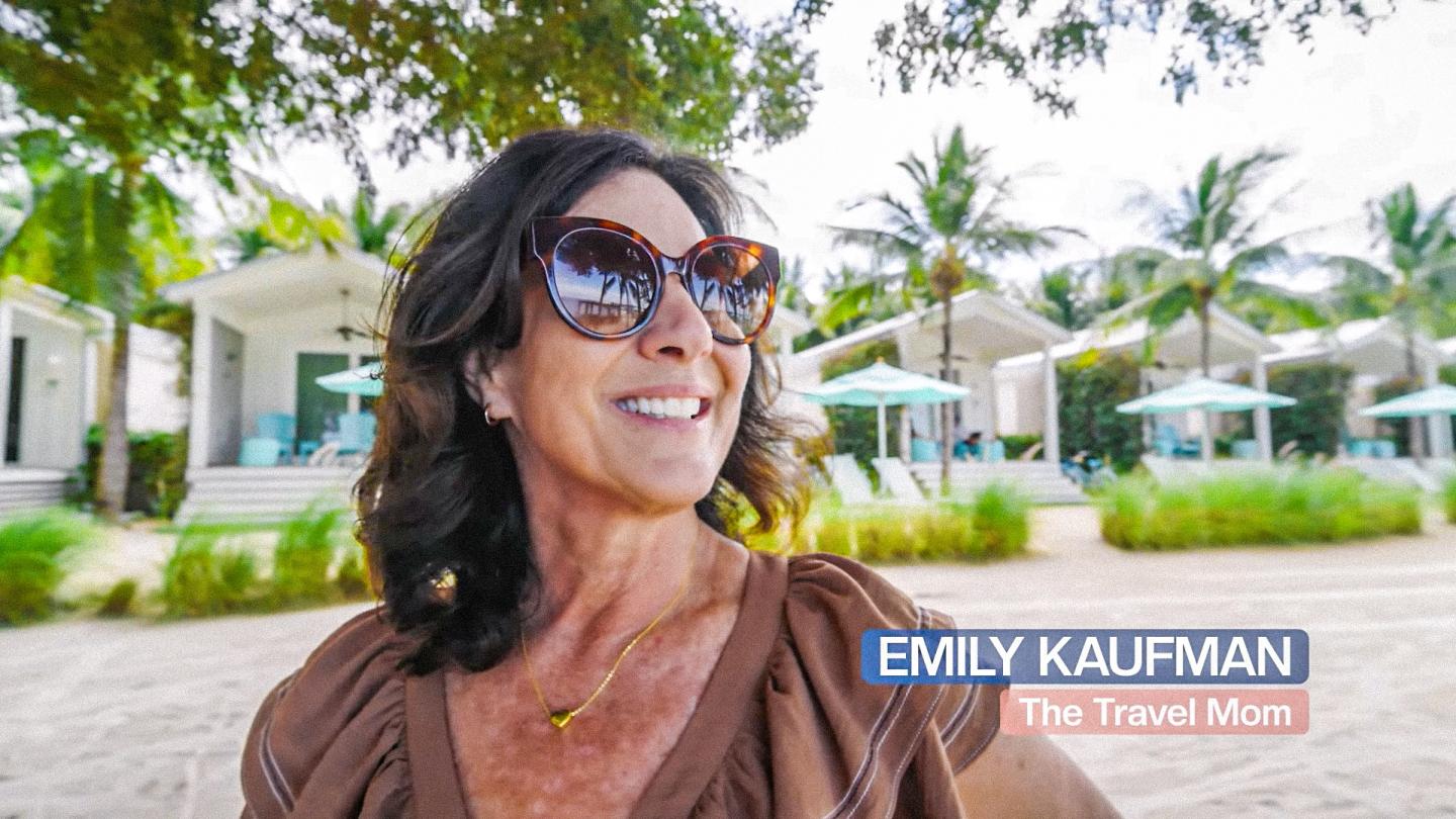 Emely Kaufman smiling outdoors at a resort, wearing sunglasses; title reads “The Travel Show.”