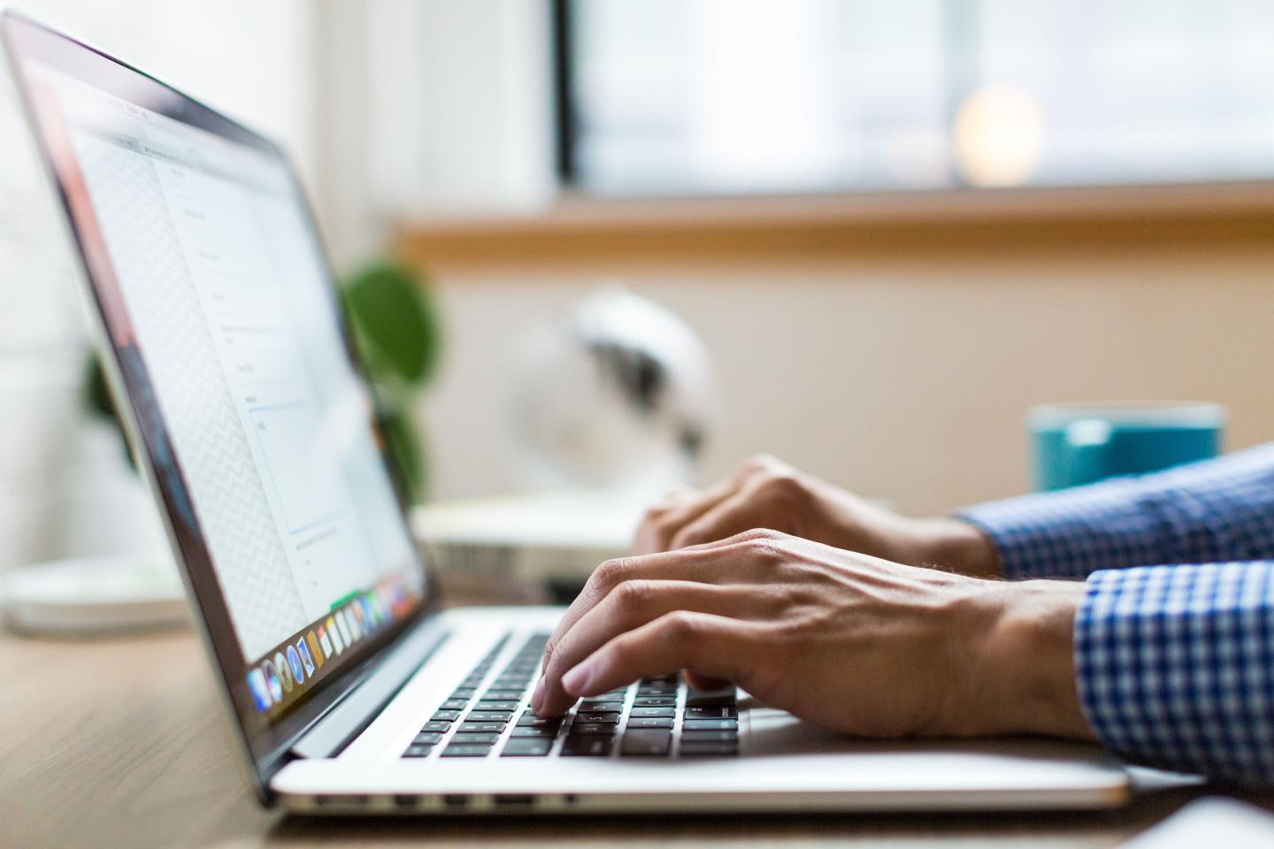 Person typing on a laptop at a desk in a bright office.