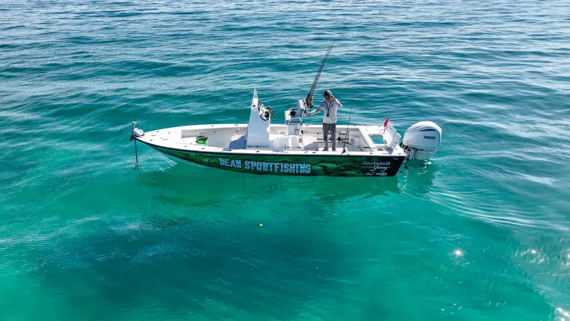 Small motorboat with two people floating on clear turquoise ocean water.