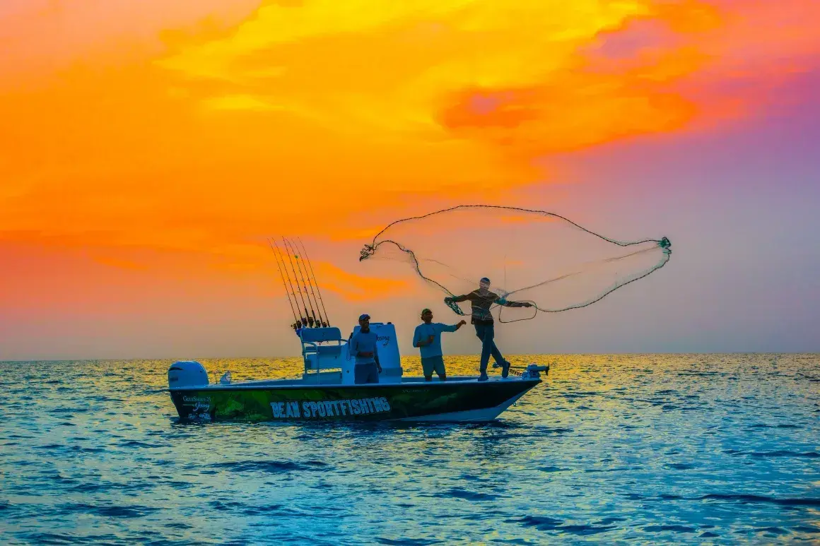 Silhouetted fishermen cast nets from a small boat at sunset.