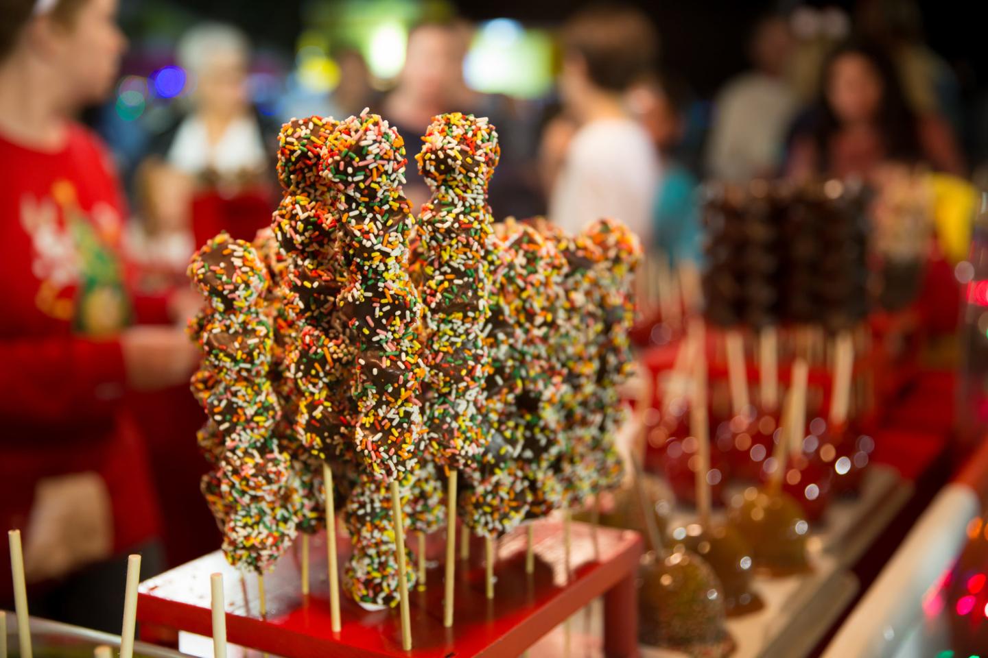Colorful sprinkle-covered cake pops on sticks at a dessert display.