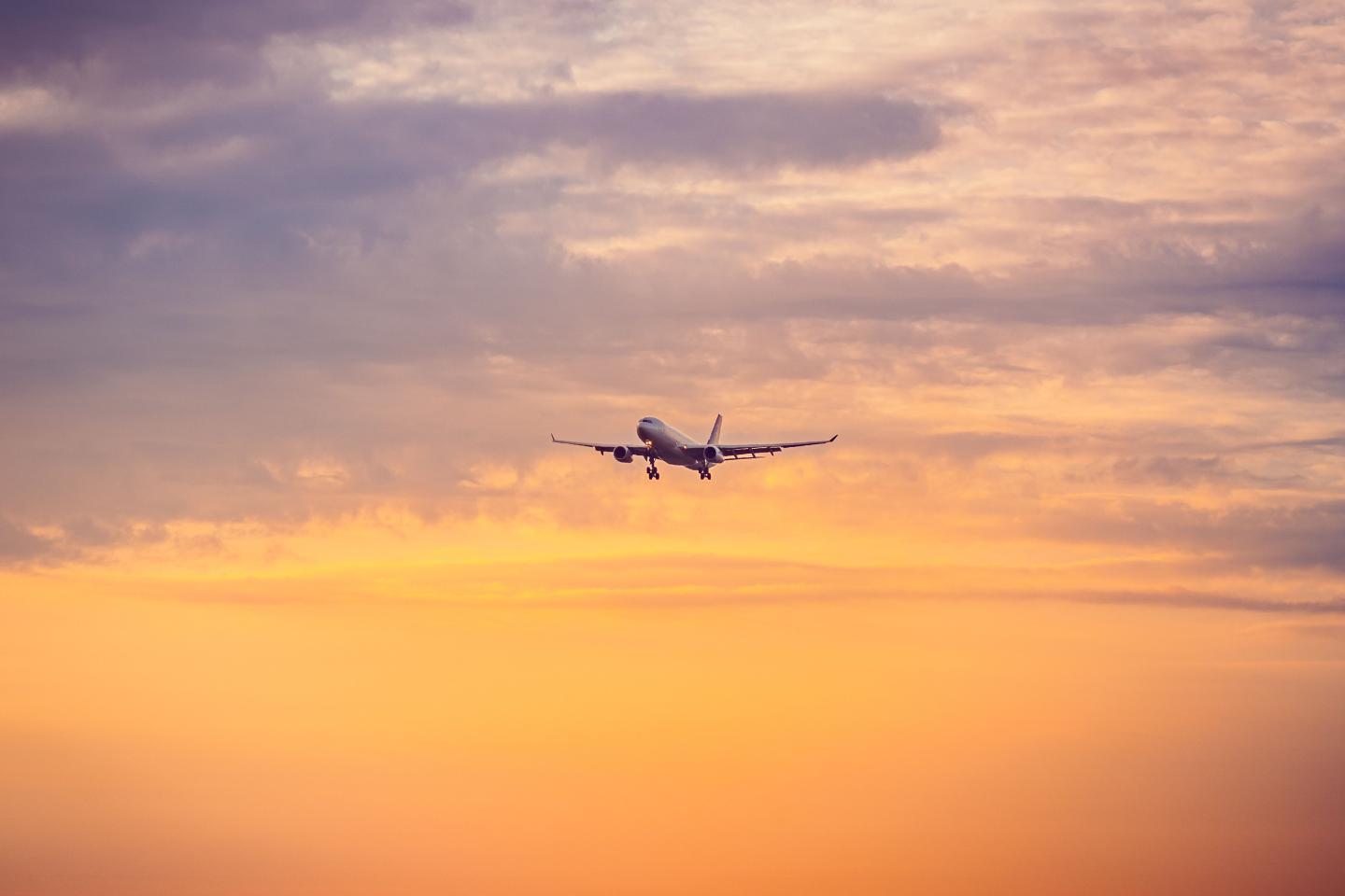 Airplane silhouetted against a golden sunset sky with layered clouds.