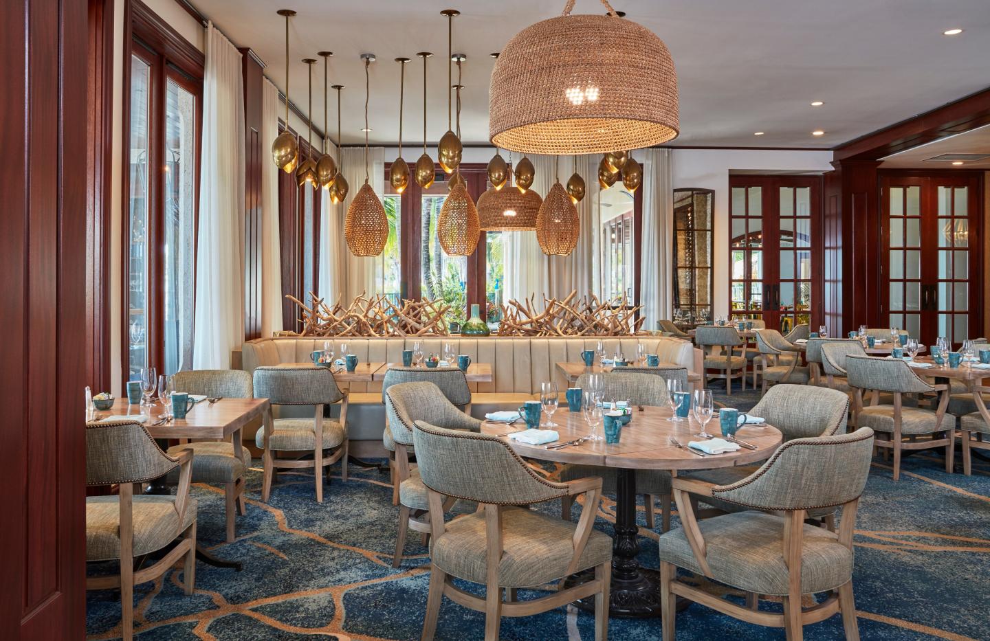 Elegant restaurant dining room with blue chairs, set tables, and woven pendant lights.