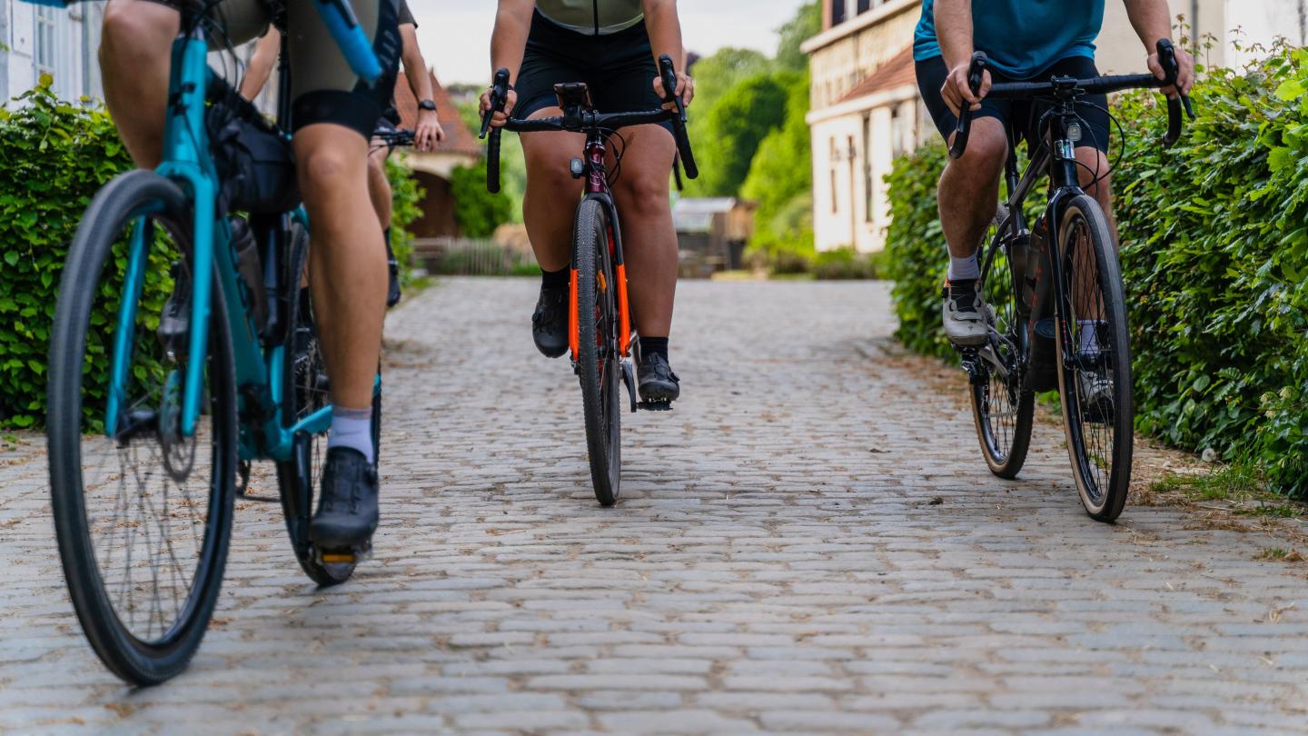 Three cyclists riding on a cobblestone street, viewed from behind.