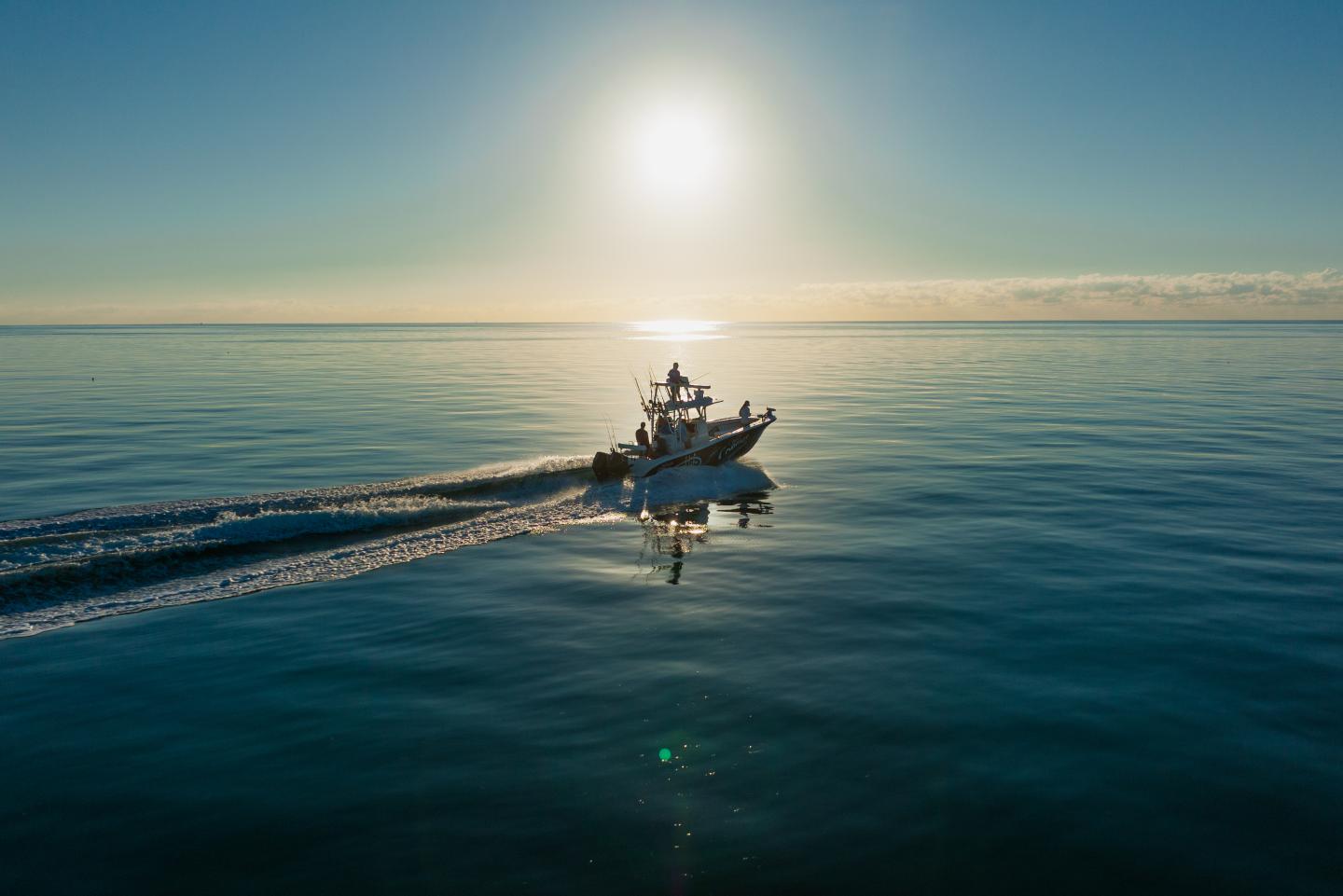 Small fishing boat crossing calm sea beneath a low sun.