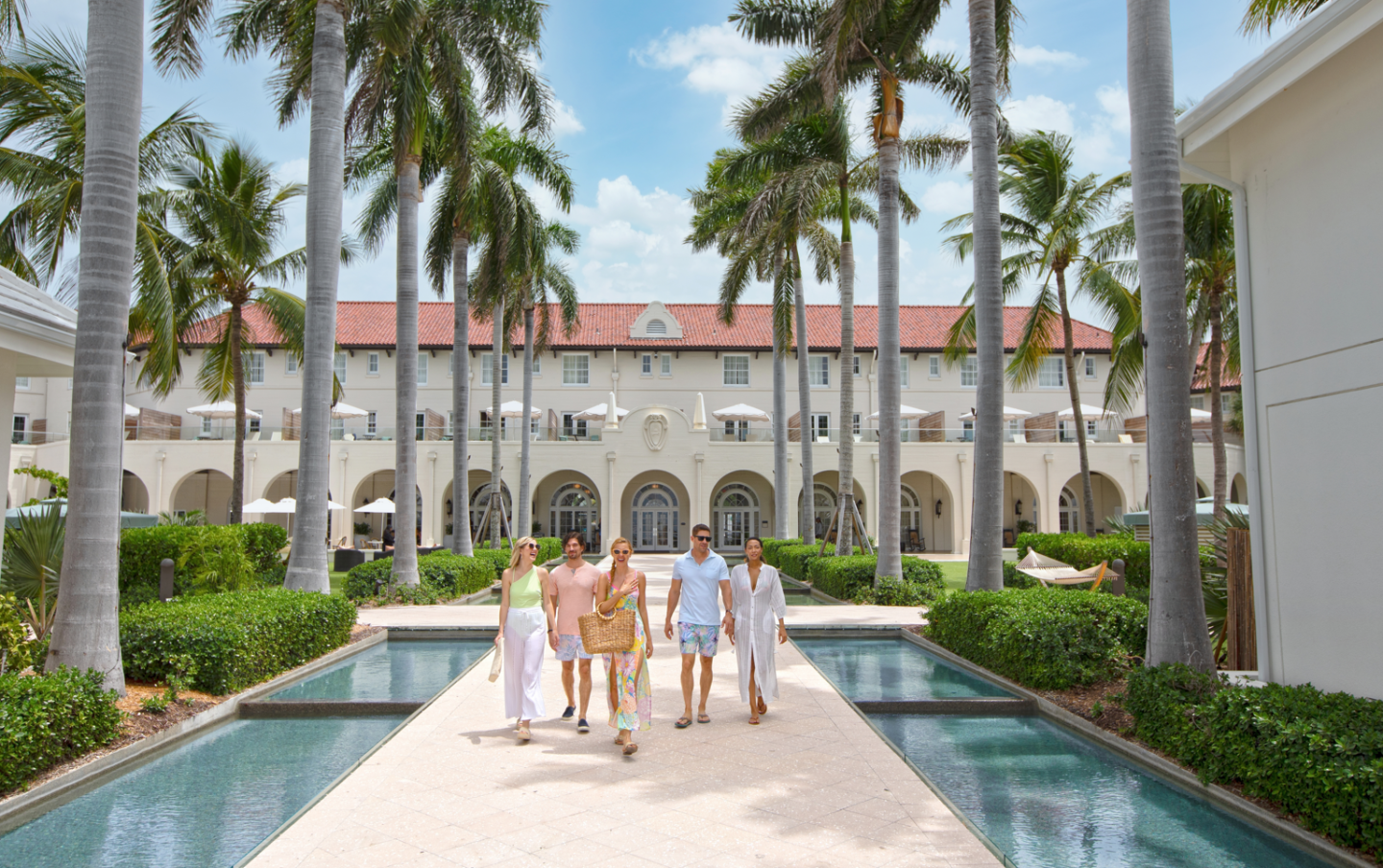 Luxury resort courtyard with palm trees, reflecting pools, and guests walking toward arches