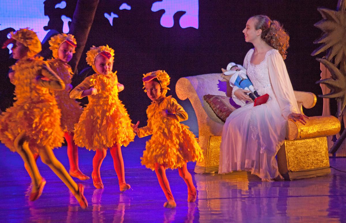Ballet dancers in orange costumes perform around a seated woman in white.