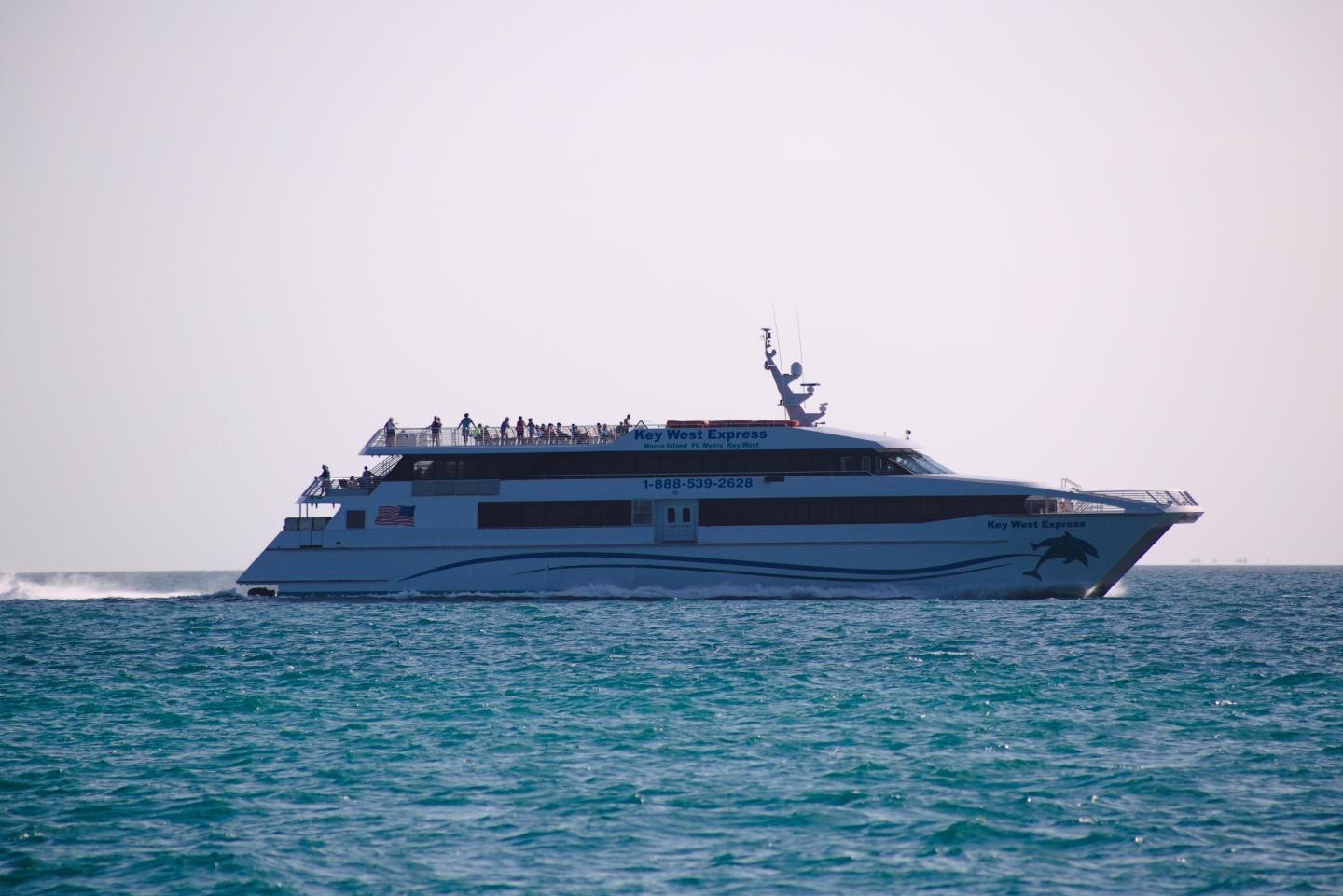 White cruise ship sailing on turquoise ocean under a pale sky.