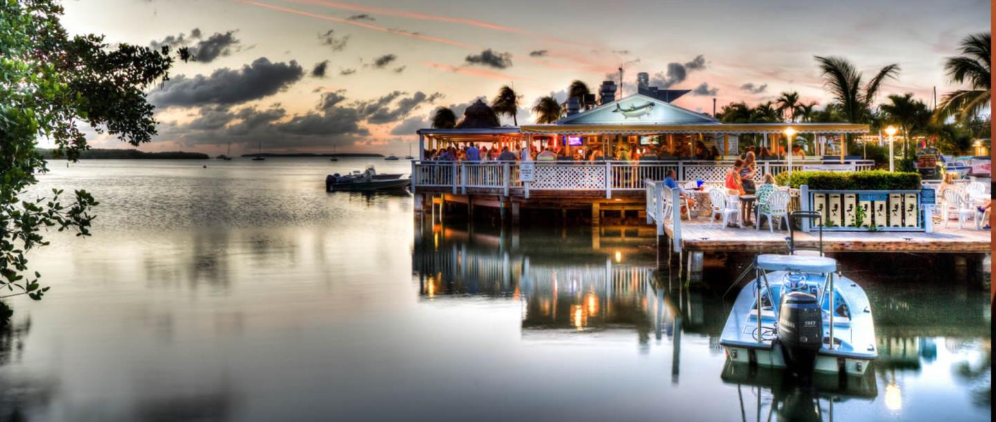 Colorful riverside restaurants reflected in calm water at sunset.