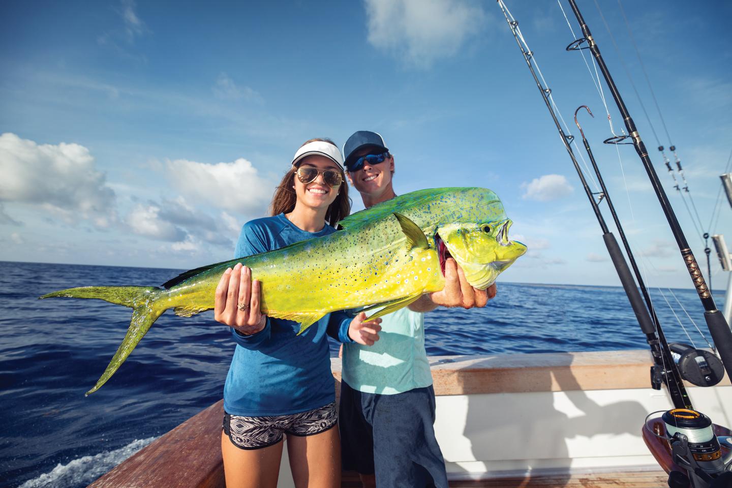 Two anglers hold a large mahi-mahi on a boat at sea.