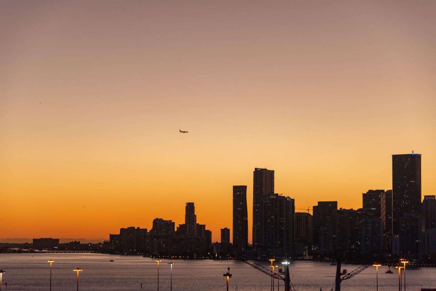 Sunset skyline of a city with dark high-rises reflected on calm water.