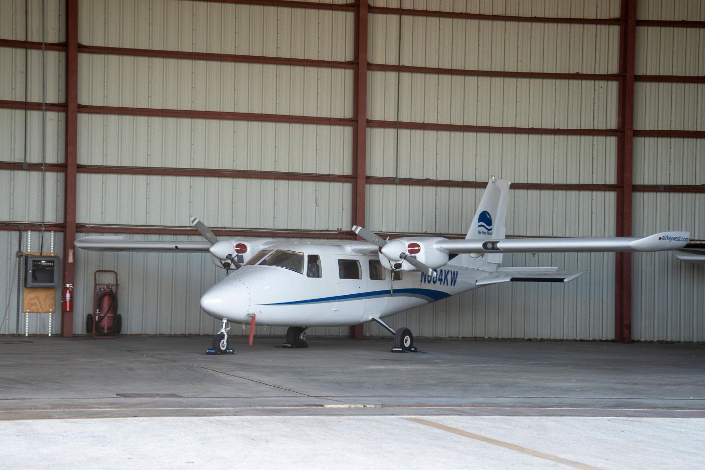 Small white aircraft parked inside a large hangar.