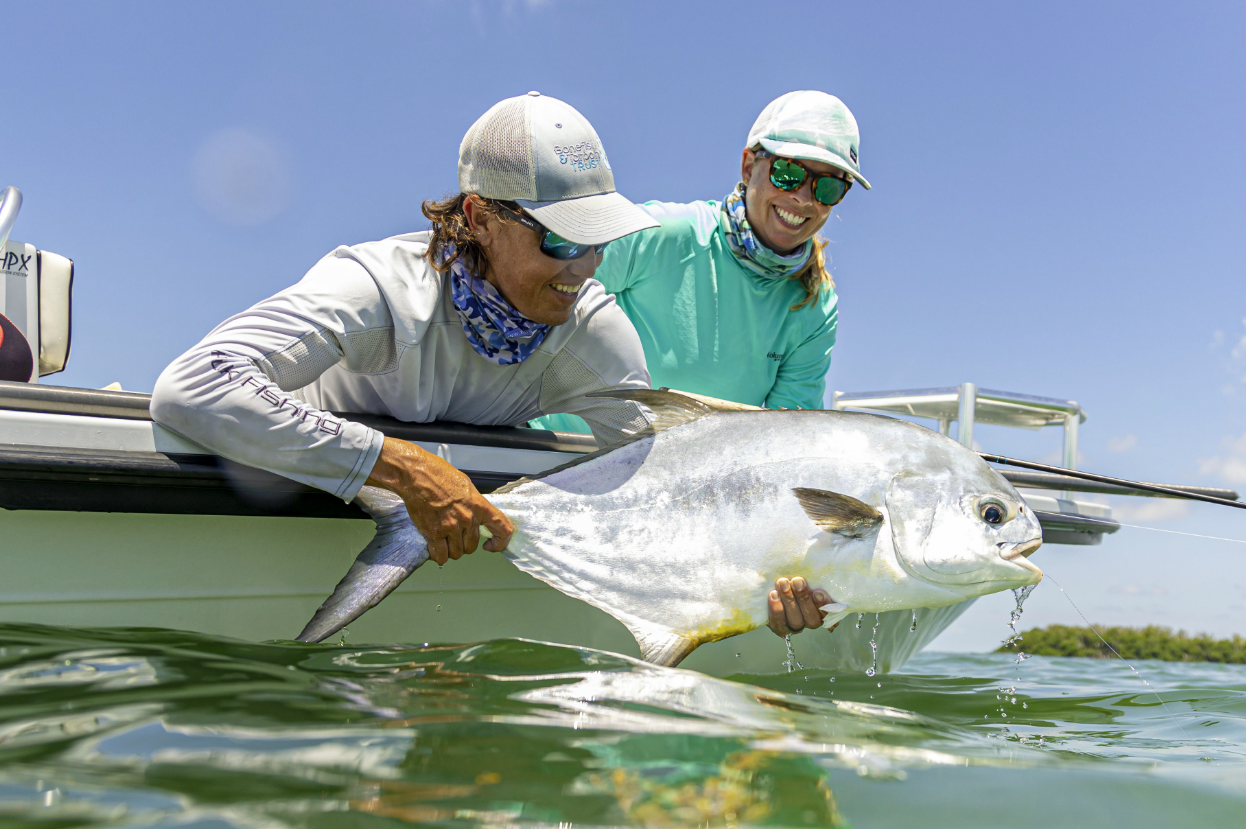 Two anglers release a large tarpon beside their boat.