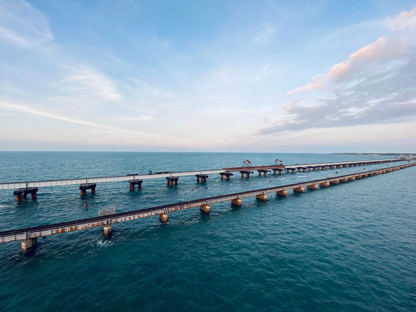 A long pier stretches across calm blue ocean beneath a cloudy sky.