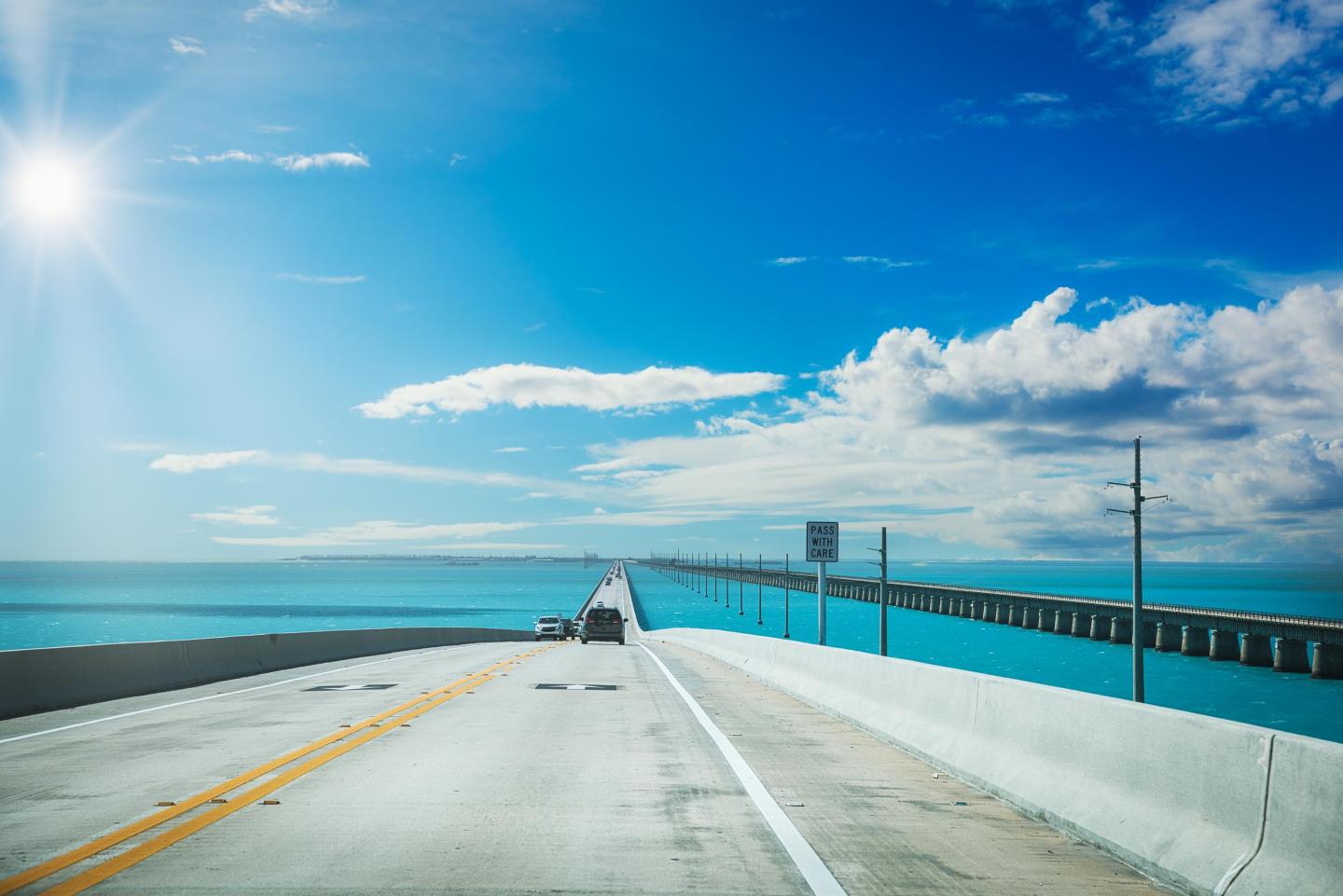 Sunny coastal bridge with turquoise railings under blue skies.