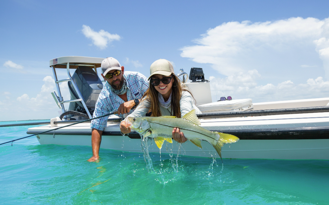 Two people holding a large fish beside a boat in clear turquoise water.