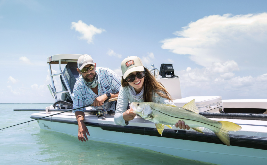 Two people in a small boat holding a large fish over clear water.