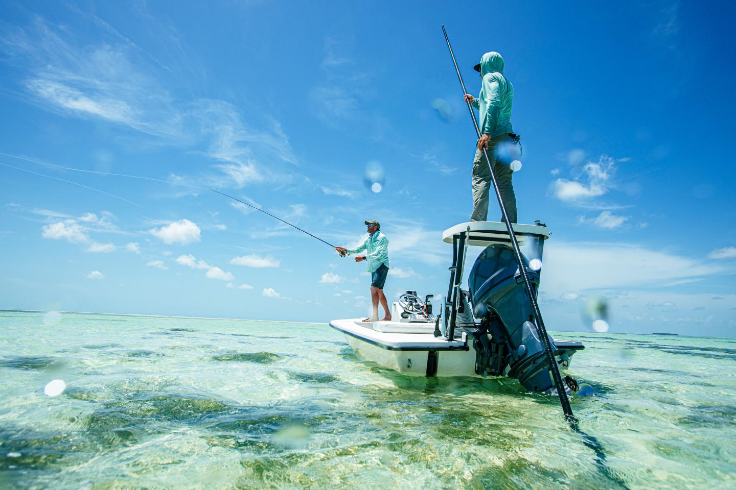 Two people on a small boat in clear turquoise shallows under a blue sky.