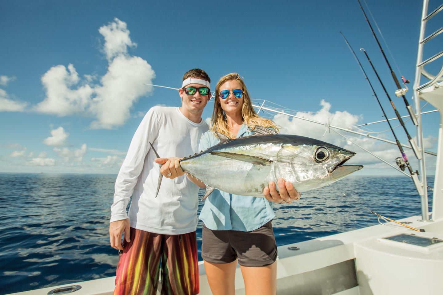 Couple on a boat holding a large tuna over the ocean.