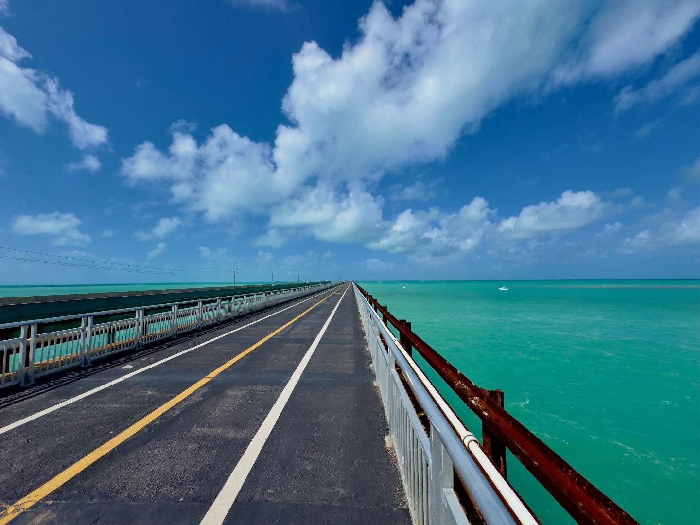 Long bridge stretching over turquoise ocean beneath a cloudy blue sky.