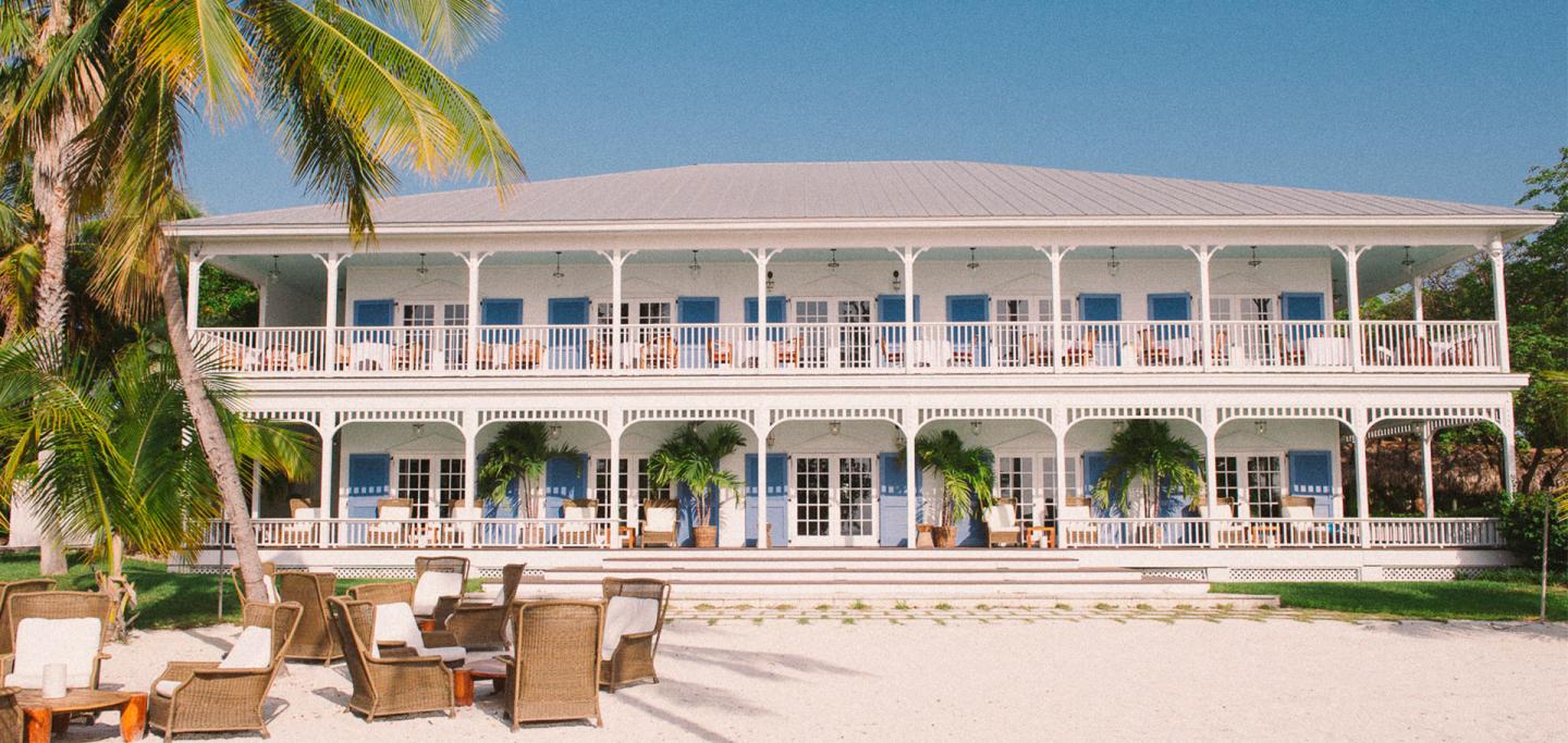 Beachfront resort with palm trees, white balconies, and lounge seating.